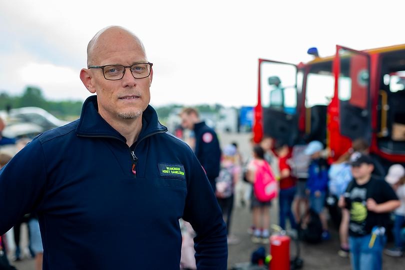 Henry Danielsson är brandman och står framför en brandbil och barn.