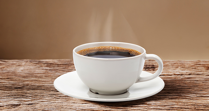 Kopp med svart kaffe står på ett träbord